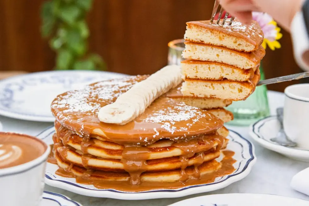 Пышные панкейки с карамельным соусом и бананом, поданные к завтраку с чашкой кофе